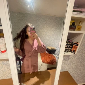 Rosa omlottklänning med puffärmar från Boohoo - Säljer en snygg rosa omlottklänning från Boohoo med puffiga långa ärmar och knyt i midjan. Klänningen har v-ringning och en figurnära passform som framhäver siluetten. Perfekt för dig som vill sticka ut lite extra!