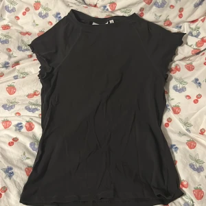 Svart topp med volangärm från Weekday - Säljer en svart topp från Weekday med korta volangärmar och rund halsringning. Toppens material känns mjukt och stretchigt, perfekt för en stilren look. Passar bra till både jeans och kjol 🫶🏼🫶🏼