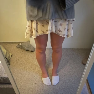 Vit volangkjol med blommigt mönster - Supersöt vit kortkjol med volanger och blommigt mönster. Kjolen har resår i midjan och är luftig i modellen, perfekt för sommaren. 🩷🩷
