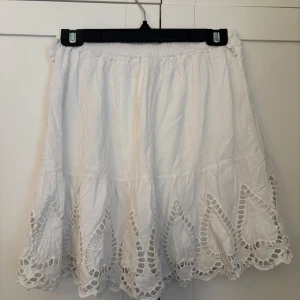 Vit kjol med broderade detaljer - Säljer en vit kortkjol med bred resår i midjan och vackra broderade spetsdetaljer längs nederkanten. Kjolen har en luftig och lätt känsla, perfekt för varma dagar. Tillverkad i Italien.