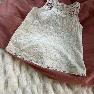 Vit spetslinne från Vintage Stories by KappAhl - Säljer ett vitt linne i spets från Vintage Stories by KappAhl. Toppen har ett vackert spetsmönster och är ärmlös med rund halsringning. Perfekt för sommardagar och lätt att matcha med olika outfits.