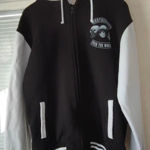 Svart och vit hoodie från Urban Classics - En hoodie som är köpt på Sellpy, har aldrig använts av mig men vad jag själv kan se så är den i god skick. Den är svart och vit frånUrban Classics hoodie med dragkedja.  Hoodien har tryck både fram och bak. På framsidan finns ett tryck med texten "Brotherhood Fuck the World" och på baksidan ett tryck med texten "No Fight No Glory". Storlek XL, nytvättad inför leverans.   B ungefär 17 cm och L 26 cm. För fler frågor eller funderingar så tveka ej att skriva!