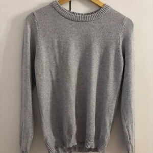 Ljusgrå stickad tröja från VILA - Mysig ljusgrå stickad tröja från VILA med rund halsringning och ribbade muddar vid ärmslut och nederkant. Perfekt för lager-på-lager och enkel att matcha med olika outfits.