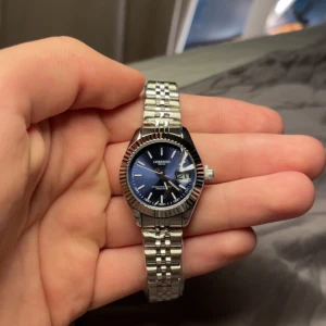 Lorenzo Milano klocka med blå urtavla - Säljer en stilren Lorenzo Milano klocka med blå urtavla och datumvisning. Klockan har ett klassiskt silverfärgat länkarmband i metall och markerad vridring. Levereras i originalask. OBS! Sprillans ny därmed är plasten på klockan kvar! Originalpris 1695kr!