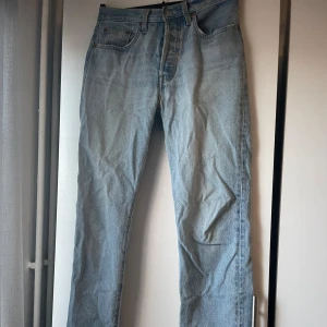 Levis 501 ljusblå jeans - Klassiska Levis 501 jeans i ljusblå denim med raka ben och knappgylf. Byxorna har fem fickor och den ikoniska Levis-lappen bak i midjan. Perfekta för en avslappnad och tidlös stil💕💕
