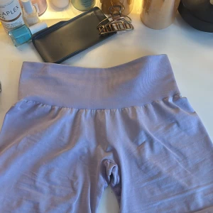 Ljuslila NVGTN shorts / gymshorts - Säljer ett par ljuslila shorts med bred ribbad hög midja. Perfekta för träning eller yoga, i mjukt och stretchigt material som sitter skönt på kroppen. Modellen är tight och slutar mitt på låret. Bär S/M i shorts därav var dehär shortsen i XS för tighta på mig.