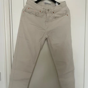 Beige jeansbyxor från Zara - Snygga beige jeansbyxor från Zara med klassisk femficksdesign och raka ben. Byxorna har silverfärgad knapp och detaljer i kopparfärg vid fickorna. Perfekta för en stilren och enkel look. Mått: 80cm (midja), 94cm (längd utsida), 66cm (längd insida).