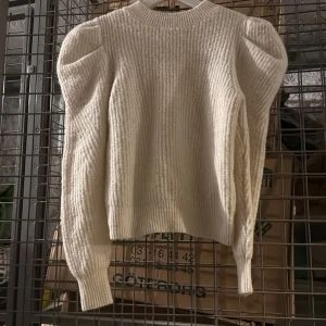 Beige stickad tröja med puffärmar från VILA - Säljer en beige stickad tröja från VILA med puffade axlar och långa ärmar. Tröjan har ribbade muddar och en rund halsringning. Perfekt för dig som vill ha en trendig och mysig look.