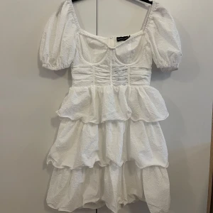 Vit volangklänning med puffärmar - Superfin vit kortklänning med puffärmar och flera lager volanger. Klänningen har markerad byst och fyrkantig urringning, perfekt till studenten 