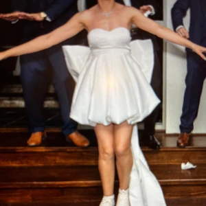 Vit axelbandslös klänning med stor rosett - Superunik vit axelbandslös klänning med en enorm rosett bak och ballongformad kjol. Klänningen har en hjärtformad byst och en lång släpdetalj baktill. Perfekt för dig som vill sticka ut på festen!