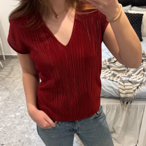 Röd plisserad topp med v-ringning - Säljer en röd plisserad topp från mango. Toppen har korta ärmar, v-ringning och är i ett lätt material. Mycket bra skick! 