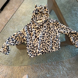 Leopardmönstrad hoodie med öron från H&M - Supermjuk och fluffig hoodie från H&M med leopardmönster och söta öron på huvan. Perfekt för dig som vill sticka ut och hålla dig varm. Tröjan är croppad och har långa ärmar.