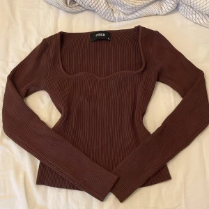 Brun ribbad topp från Cider - Säljer en brun långärmad topp från Cider med ribbad struktur och fyrkantig urringning. Toppen har en figurnära passform och är tillverkad i stretchigt material som sitter snyggt på kroppen. Perfekt för lager-på-lager eller som den är.