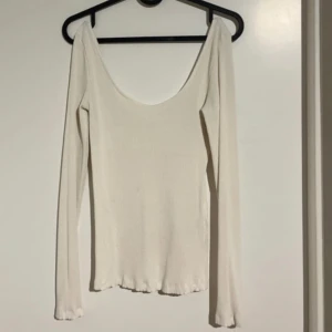 Vit ribbad långärmad topp - Säljer en vit långärmad topp med djup urringning fram men även bak och ribbad struktur. Toppen är figurnära och har en enkel, stilren design som passar till många olika outfits.