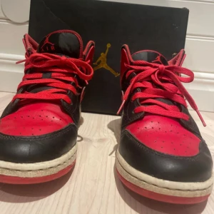 Nike Air Jordan 1 Bred sneakers - Säljer ett par ikoniska Nike Air Jordan 1 Bred sneakers i svart och rött skinn med klassisk röd swoosh och snörning. Skorna har rund tå, platt sula och mids höjd. Perfekt för dig som vill ha en streetstyle-vibe med retro känsla. Box medföljer.