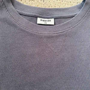 Grå långärmad tröja från Kappahl - Säljer en stilren grå långärmad tröja från Kappahl i storlek 170. Tröjan är tillverkad i 100% bomull och har en ribbad, strukturerad yta som ger en cool och avslappnad vibe. Perfekt för dig som gillar enkel och bekväm stil.