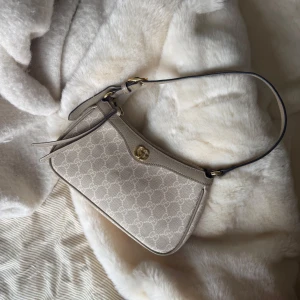 Ophidia Small Handbag - Elegant väska med det ikoniska GG-mönstret och en justerbar axelrem. Väskan har en tidlös design med guldfärgade detaljer och en dragkedja. Köpt second hand utan äkthetsbevis. Kvitto från Vestiaire Collective, där tidigare ägare köpt väskan finns.