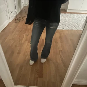 Blå bootcut jeans med slitningar - Snygga blå jeans med bootcut-modell och slitna detaljer framtill. Jeansen har låg midja, klassiska fickor och stängs med dubbla knappar. Perfekta för dig som gillar en avslappnad men trendig look.