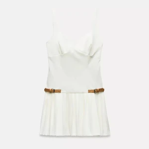 Vit Zara klänning  - Supersnygg vit kortklänning från Zara med breda axelband och v-ringad urringning. Kjolen är plisserad och har två bruna bältesdetaljer i midjan som ger en cool kontrast. Klänningen är figurnära upptill och har en snygg look. Finns inte kvar på hemsidan, aldrig använd prislappen sitter kvar. Köpt för 500 kr💞