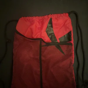 Mörkrosa och svart gympåse med meshficka - Säljer en mörkrosa gympåse med svarta detaljer och snörstängning. Framsidan har en stor svart grafisk detalj ( märket SOC)  och en meshficka för extra förvaring. Perfekt för att slänga ner träningskläder eller skor. Lätt och smidig att bära på ryggen med svarta snören. Dock har loggan flacknat av lite så har sänkt på priset. 