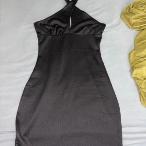 Svart omlottklänning från H&M Divided - Snygg svart kortklänning från H&M Divided med omlottdetalj vid halsen och ribbad struktur. Klänningen är ärmlös och har en figurnära passform som framhäver siluetten. Perfekt för dig som gillar stilrena och trendiga plagg.