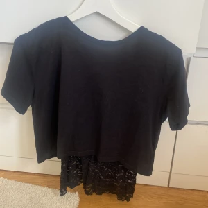 Svart topp med spets från Gina Tricot - Snygg svart topp från Gina Tricot med korta ärmar och croppad passform. Nederdelen har en cool spetsdetalj som ger extra edge till looken. Perfekt för dig som gillar att sticka ut med stilrena detaljer och enkel design.