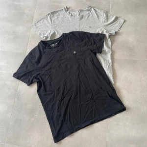 Svart och grå t-shirt Jack & Jones M - Två stilrena t-shirts från Jack & Jones Originals i storlek M. Ena är svart och den andra ljusgrå, båda med rund hals och diskret broderad logga på bröstet. Mjukt bomullsmaterial och klassisk passform, perfekta för chill och enkel stil.