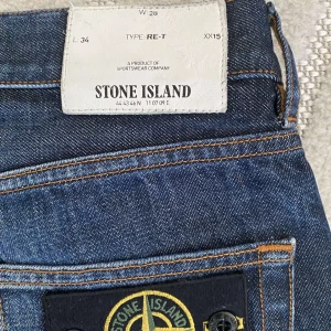 Stone Island blå jeans W28 L34 - Snygga blå jeans från Stone Island med klassisk patch på bakfickan och tydliga kontrastsömmar. Jeansen har rak passform och är tillverkade i slitstarkt denim med cool tvättad look. Perfekta för dig som gillar streetwear och vill sticka ut lite extra.