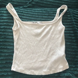 Vit ribbad linnetopp från NA-KD - Säljer en stilren vit ribbad linnetopp från NA-KD. Toppen har smala axelband och är figurnära med en enkel, rak skärning. Perfekt att matcha med jeans eller kjol för en clean look.