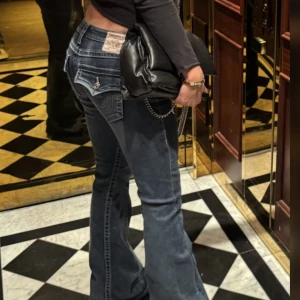 True Religion bootcut jeans - Säljer ett par ikoniska True Religion Joey jeans i blå denim med kontrastsömmar och snygga fickdetaljer. Modellen har låg midja och bootcut-ben, klassisk logga på bakfickan och coola silverfärgade knappar. 