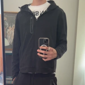 Svarta mjukisbyxor och zip tröja - Säljer ett par svarta mjukisbyxor med snörning i midjan och ribbade muddar vid bensluten. Byxorna har dragkedjeförsedda fickor på sidorna och en loose passform som är riktigt chill. Perfekta för att hänga hemma eller dra till gymmet.