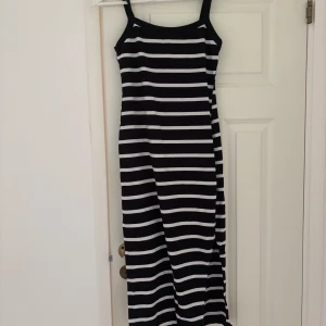 Svartvit randig långklänning - Säljer en svartvit långklänning med smala axelband och horisontella ränder. Klänningen har en rak och enkel siluett som ger en chill vibe. Perfekt för dig som gillar klassiska mönster och vill ha något bekvämt och snyggt.