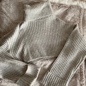 Stickad tröja  - Grå stickad tröja med polo krage och utsvängda armar. Croppad i modellen och super varm och mysig!! Säljs då d ej kommer t användning. Endast en defekt vid kragen. I storlek S. Hör av er vid flera frågor.