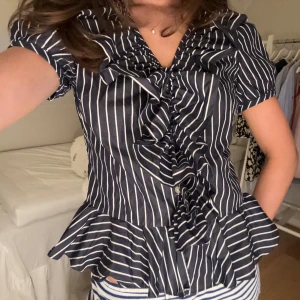 Randig blus från Ralph Lauren - Supersöt blus från Ralph Lauren i marinblått med vita ränder. Blusen har korta puffärmar, volangkant nertill och längs ringningen samt en snygg omlottkänsla framtill. Blusen är i helt nyskick!