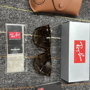 Ray-Ban Wayfarer brunmelerade solglasögon - Snygga Ray-Ban Wayfarer solglasögon i brunmelerad plast med klassisk form och mörka glas. Modellen är RB4147 och de kommer med originalfodral och putsduk. Perfekta för att lyfta din stil under soliga dagar.