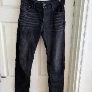Svarta jeans  - Säljer ett par svarta jeans med snygga slitningar och tvättade detaljer på låren. Från Jack & Jones, modellen heter comfort/Mike.  Klassisk femficksmodell med smal passform och raka ben. Jeansen har dragkedjegylf och är tillverkade i ett stretchigt bomullsmaterial för extra komfort.