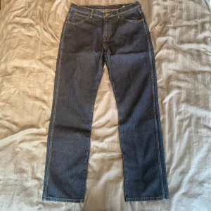 Wrangler jeans straight fit  - Stilrena wrangler jeans i ett rakt snitt. Klassisk femficksdesign med en subtil wranglerlapp i läder på bakficka. Inga täcken på slitage utöver lite tappad indigo på de vanliga ställen (ficka, gylf, skrev osv)