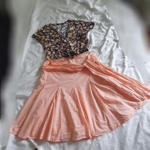 Blommig kjol från Bik Bok och Vero moda blus - Supersöt kjol  från Bik Bok i storlek M. Och Vero moda blus storlek S Överdelen är blommig med v-ringning och korta ärmar, medan kjolen är ljus persikofärgad och har snygga veck. Perfekt för dig som gillar färg och mönster! Materialet känns lätt och somrigt.