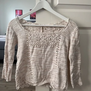 Beige stickad kofta med spetsdetaljer - Supersöt beige stickad kofta med virkade spetsdetaljer och knappar i ryggen. Koftan har lång ärm, vackert mönstrad framsida och baksida samt fina virkade kanter. Perfekt för dig som gillar romantisk och bohemisk stil.