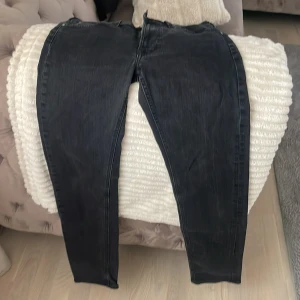 Svarta Lee jeans med smal passform - Säljer ett par svarta jeans från Lee med smal passform. Jeansen har klassisk femficksdesign, Lee-logga på knappen och etikett i midjan. Materialet är jeans och färgen är mörksvart med lätt tvättad look. Perfekta för dig som gillar stilrena och bekväma jeans.