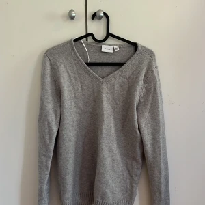 Grå stickad tröja från VILA - Snygg grå finstickad tröja från VILA i storlek XS. Tröjan har v-ringad hals, långa ärmar och ribbade muddar vid ärmslut och nederkant. Den är knappt använd och inte nopprig.