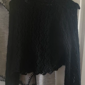 Svart spetsig långärmad tröja - Säljer en svart långärmad tröja med lång ärm och genombrutet spetsmönster. Toppen har en lätt croppad passform och vågig nederkant, perfekt för dig som gillar en lite edgy och romantisk stil. Superfin att styla med höga jeans eller kjol.