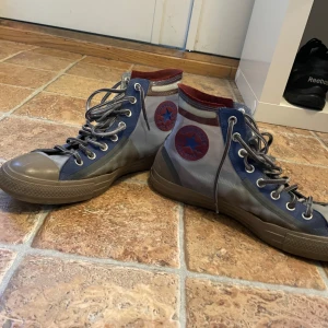 Converse All Star höga sneakers blå/grå - Unika Converse All Star high tops med transparent grå mesh, blå detaljer och bruna gummipartier. Röd insida och klassisk Converse-logga på sidan. Snygga snörningar och robust sula gör dem till ett statement i varje outfit.