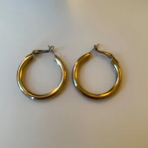 Guldiga hoops örhängen - Säljer ett par guldiga hoops örhängen med klassisk rund form. De har en enkel låsmekanism och ger en snygg statement-look. Perfekta om du gillar stilrena och trendiga accessoarer som syns. Passar till allt och är superlätta att bära.