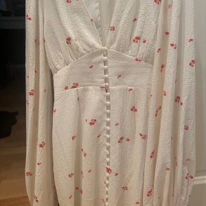 Vit kortklänning med röda blommor - Superfin vit kortklänning med små röda blommor och långa ärmar. Klänningen har en lätt v-ringning och markerad midja som ger en snygg siluett. Perfekt för sommarens alla tillfällen och ger en fräsch och söt look. Kom privat för fler bilder, klänningen är en adoore i kort modell. Så fin och endast använd 1 gång❣️