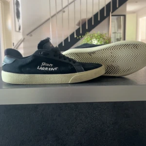 Svarta sneakers från Saint Laurent - Svarta sneakers från Saint Laurent med handskriven logga på sidan. Skorna är söndriga i sulan kan gå att använda om dom limmas