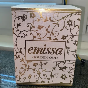 Emissa Golden Oud parfym - Lyxig parfym från Emissa i doften Golden Oud. Flaskan är ljusrosa med guldiga detaljer och har en elegant, facetterad form med genomskinlig botten och rund, kristalliknande kork. Kommer i en vacker ask med blommigt guldmönster. Perfekt för dig som gillar exklusiva dofter.