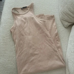 Beige ribbad klänning Zara - Säljer en enkel och stilren beige linnetopp från Zara . Toppen är ribbad och ärmlös med rund halsringning och smala axelband. Perfekt att matcha med jeans eller kjol för en avslappnad look.