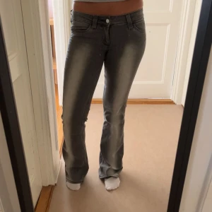 Grå bootcut jeans med slitning - Säljer ett par grå jeans med snyggt slitna detaljer och bootcut-modell. Jeansen har klassisk femficksdesign, låg midja och är tillverkade i stretchigt denimtyg för en bekväm passform. Perfekta för dig som gillar en retro vibe och vill sticka ut.