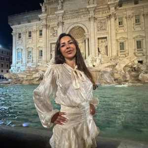 Champagnefärgad omlottklänning med volang - Säljer en superfin kort klänning i champagnefärgat, glansigt material med omlott och volangdetaljer. Klänningen har långärmade puffärmar och knyt i halsen för extra stilpoäng. Perfekt för dig som vill sticka ut med en elegant look.